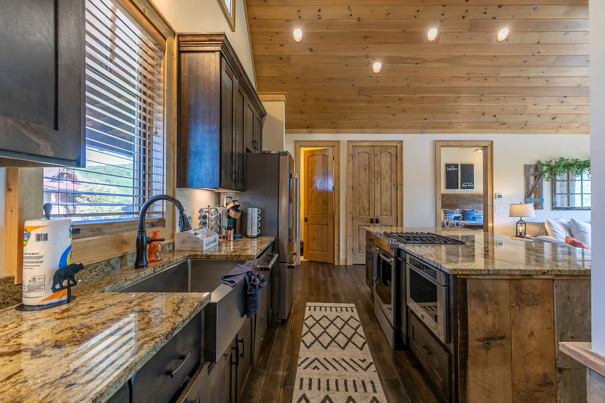 A well-appointed kitchen scene featuring granite countertops, rich wooden cabinetry, stainless steel appliances, and expansive windows that usher in natural light. The space is designed for both cooking and entertaining, with ample room for gathering and celebrating special moments.