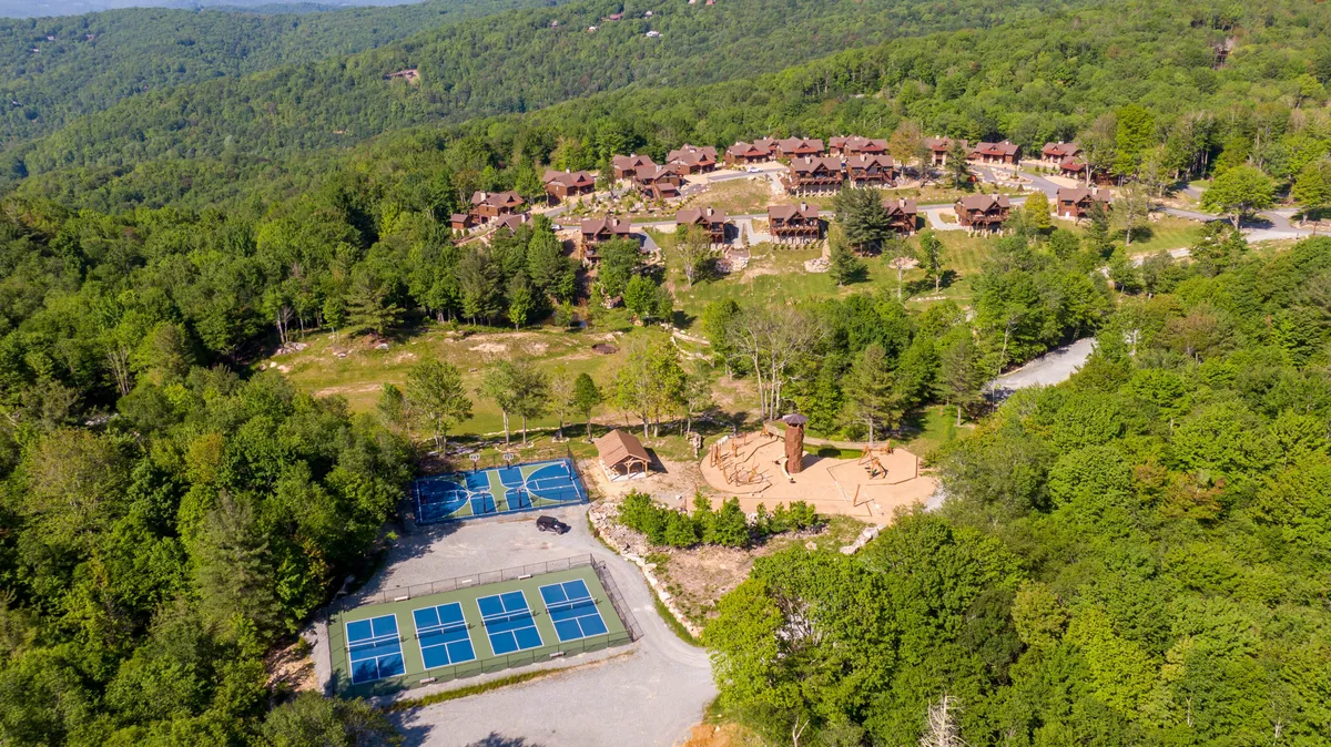 A relaxed exterior view of cabins nestled in the forest, with tennis courts, a play area for children, and winding walking paths. Families are seen enjoying the outdoors and engaging in activities together.