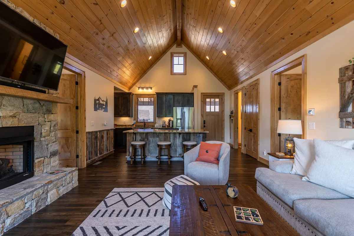 A welcoming living space featuring a stone fireplace and vaulted wooden ceiling, with a comfortable seating area perfect for relaxing after outdoor adventures. Large windows hint at the outdoors, linking the cozy interior with the surrounding natural environment.