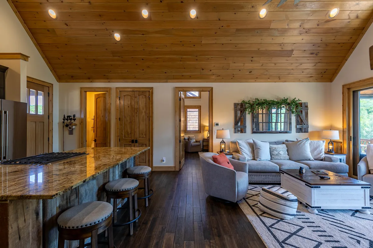 This image features a spacious, open-concept living area with a granite kitchen island, comfortable seating, and decorative accents. The layout invites group gatherings and casual entertaining, reflecting a lively yet relaxed atmosphere. Large windows hint at outdoor views, subtly connecting the interior to the exterior surroundings.