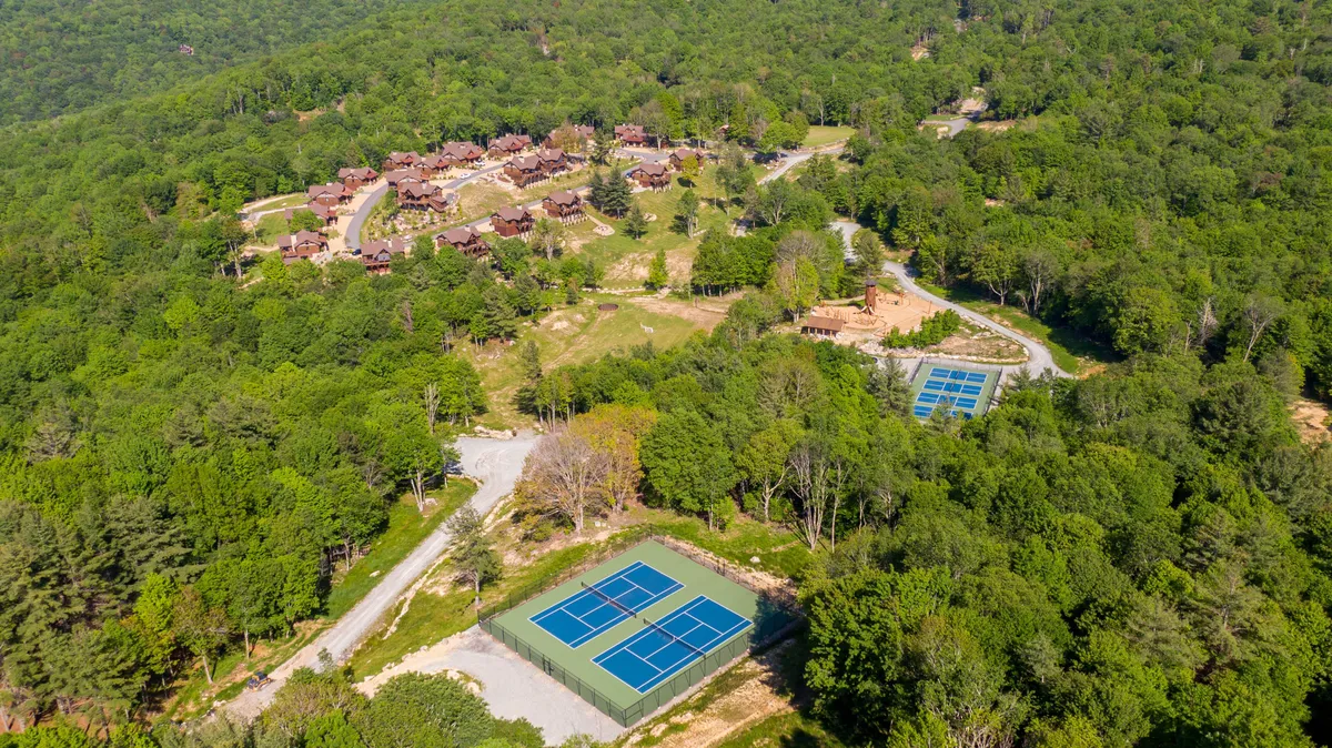 A sweeping view of residential buildings set amid lush trees, with tennis courts visible in the foreground. The setting evokes an active, community-oriented environment perfect for recreation and gatherings.