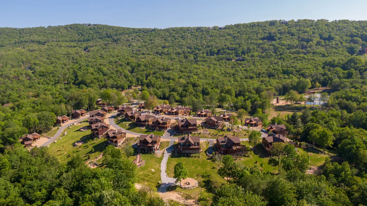 A cluster of cozy cabins nestled among greenery with winding pathways and a serene water feature. Community spaces invite outdoor gatherings, nature walks, and stargazing, creating a welcoming, communal atmosphere.