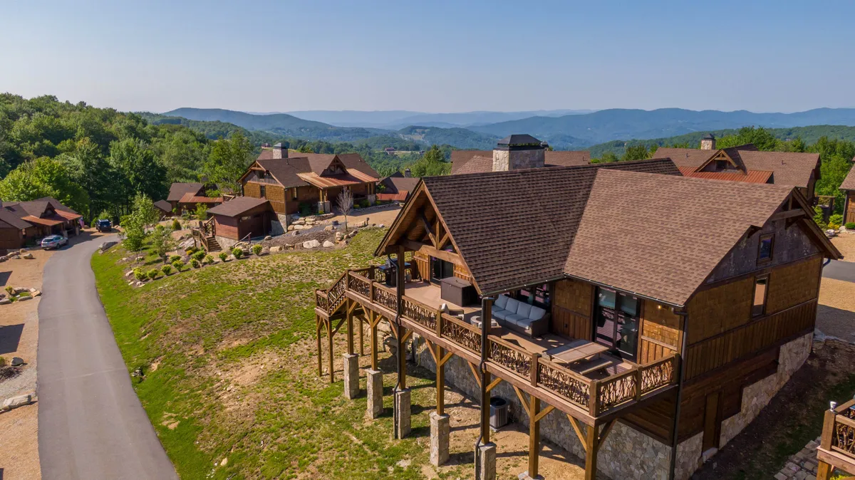The hero image spotlights a charming wooden cabin nestled against a backdrop of sweeping Blue Ridge mountains, with an expansive deck overlooking the scenery. Cozy outdoor furniture invites guests to relax as the sun sets, painting the sky in vibrant hues, while the tranquil wilderness frames the perfect setting for both morning coffee and starlit evenings.