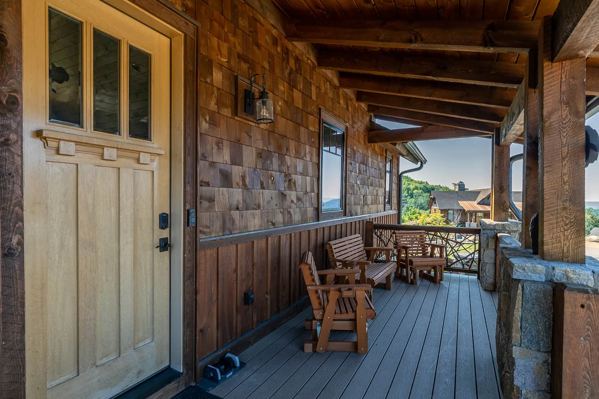 A charming view of the front porch with wooden rocking chairs and a stone railing, inviting relaxation and socializing in the fresh mountain air. While this image focuses on the front rather than the back deck, it effectively conveys the experience of savoring coffee outdoors, enjoying sunsets, and the overall tranquil outdoor lifestyle highlighted in the section.