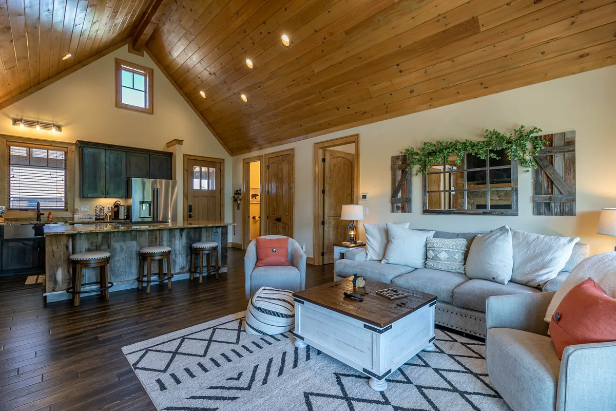 A cozy living room with a sofa, coffee table, and open kitchen island, all set under a rustic wooden ceiling. The space is designed for socializing, relaxing, and enjoying time with family or friends after active pursuits.
