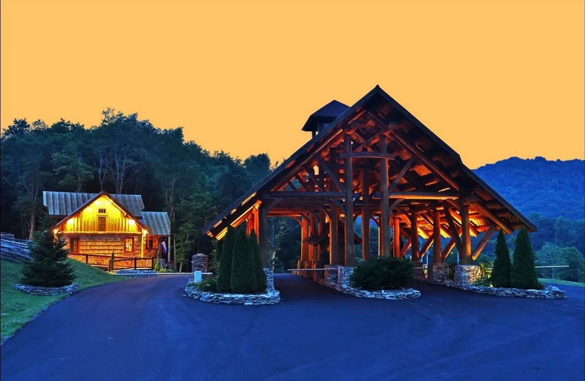 A cozy cabin and a large wooden structure are illuminated along a pathway at dusk, set against a backdrop of natural beauty. The scene hints at stargazing opportunities and peaceful evenings spent outdoors with friends or loved ones.